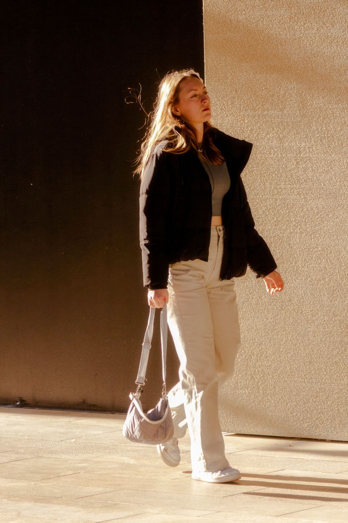 contact-img Stylish young woman walking confidently with a handbag under bright sunlight.