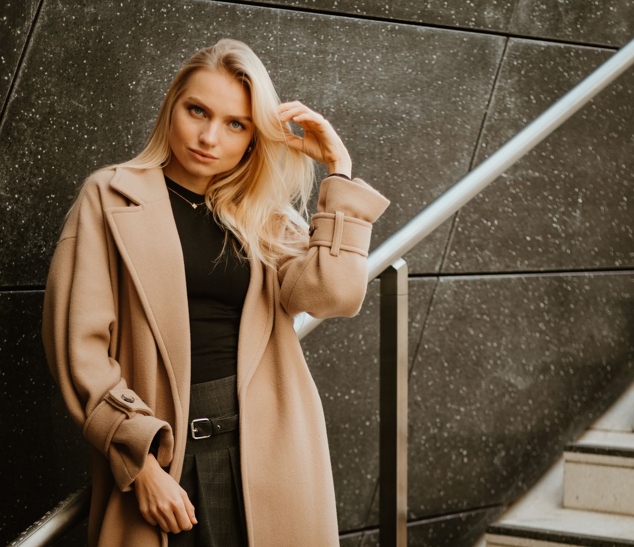 about-img Fashionable woman in a beige coat posing on a modern staircase in an urban setting.