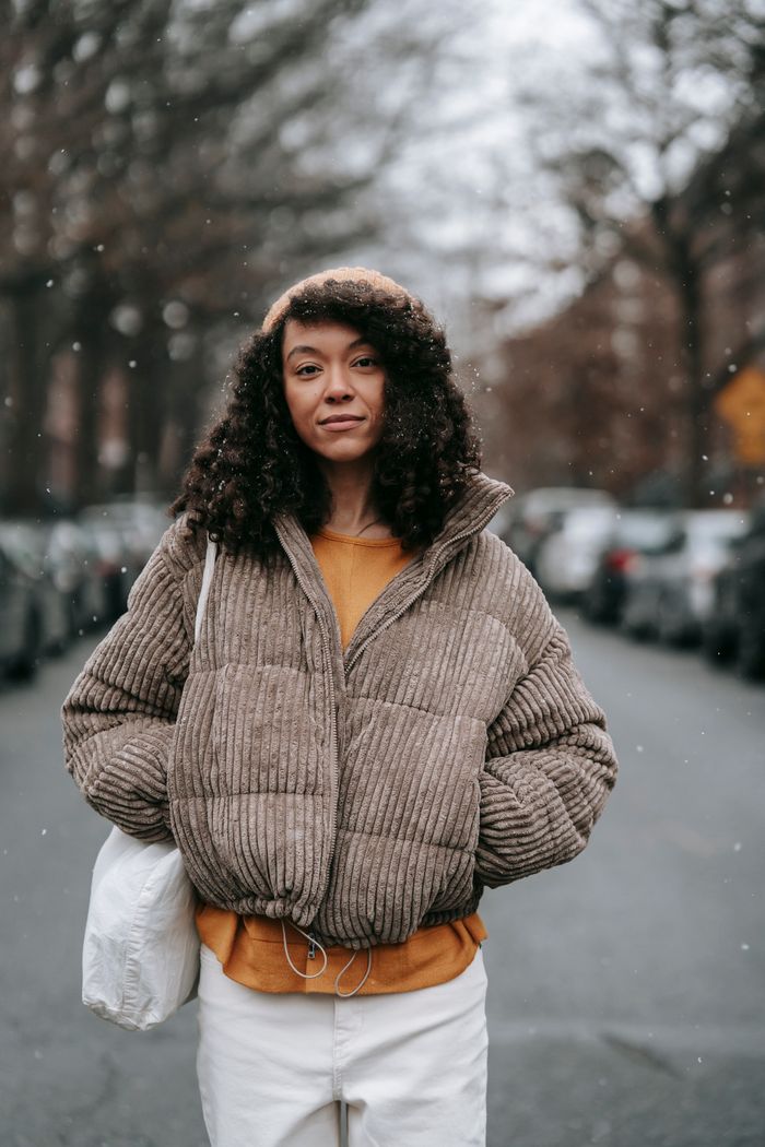 our-experience Confident African American female in trendy warm clothes with hands in pockets looking at camera on urban roadway in snowfall